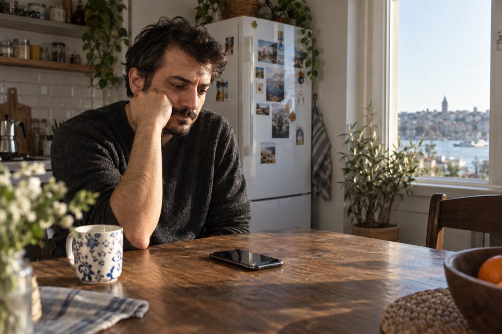 Mutfak masasında telefonunu yanına koymuş düşünceli biçimde bekleyen erkek